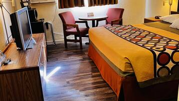 A hotel room with a bed, a desk with a computer, a chair, a small table, and a window with curtains.