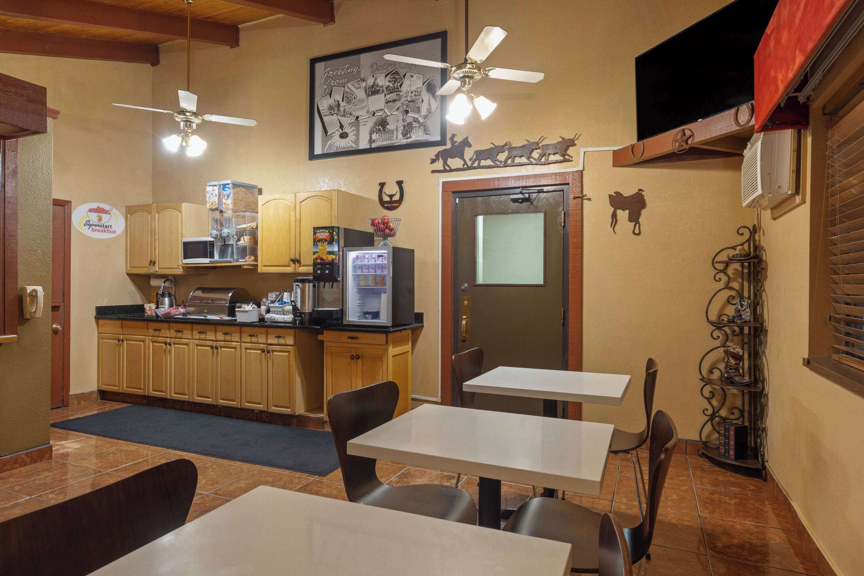 A restaurant with a counter, tables, and chairs. There is a ceiling fan, a refrigerator, and a microwave on the counter.
