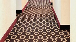 A hotel hallway with a patterned carpet, white walls, and a red carpet border. - Super 8 by Wyndham Dodge City (Dodge City)