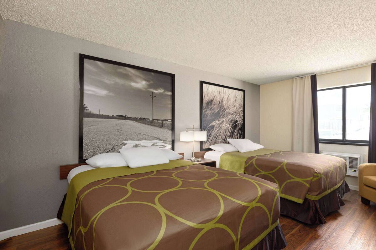 A hotel room with two beds, a large window, and artwork on the walls.