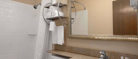 A bathroom with a white bathtub, a sink with a granite countertop, a mirror with a gold frame, and a towel rack with folded towels.