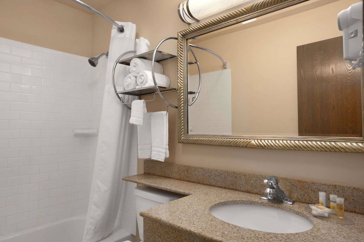A bathroom with a shower, a sink with a granite countertop, a mirror with a decorative frame, and towels on a rack.