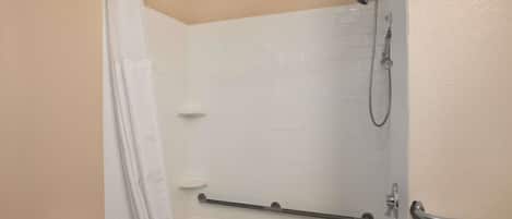 Ein Badezimmer mit Dusche, einer Haltestange, einem Handtuchhalter und einer Toilette.