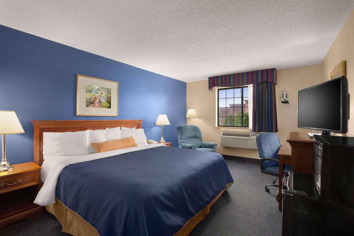 A hotel room with a large bed, two bedside tables with lamps, a desk with a television, and a window with curtains.