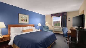 A hotel room with a large bed, two bedside tables with lamps, a desk with a television, and a window with curtains.