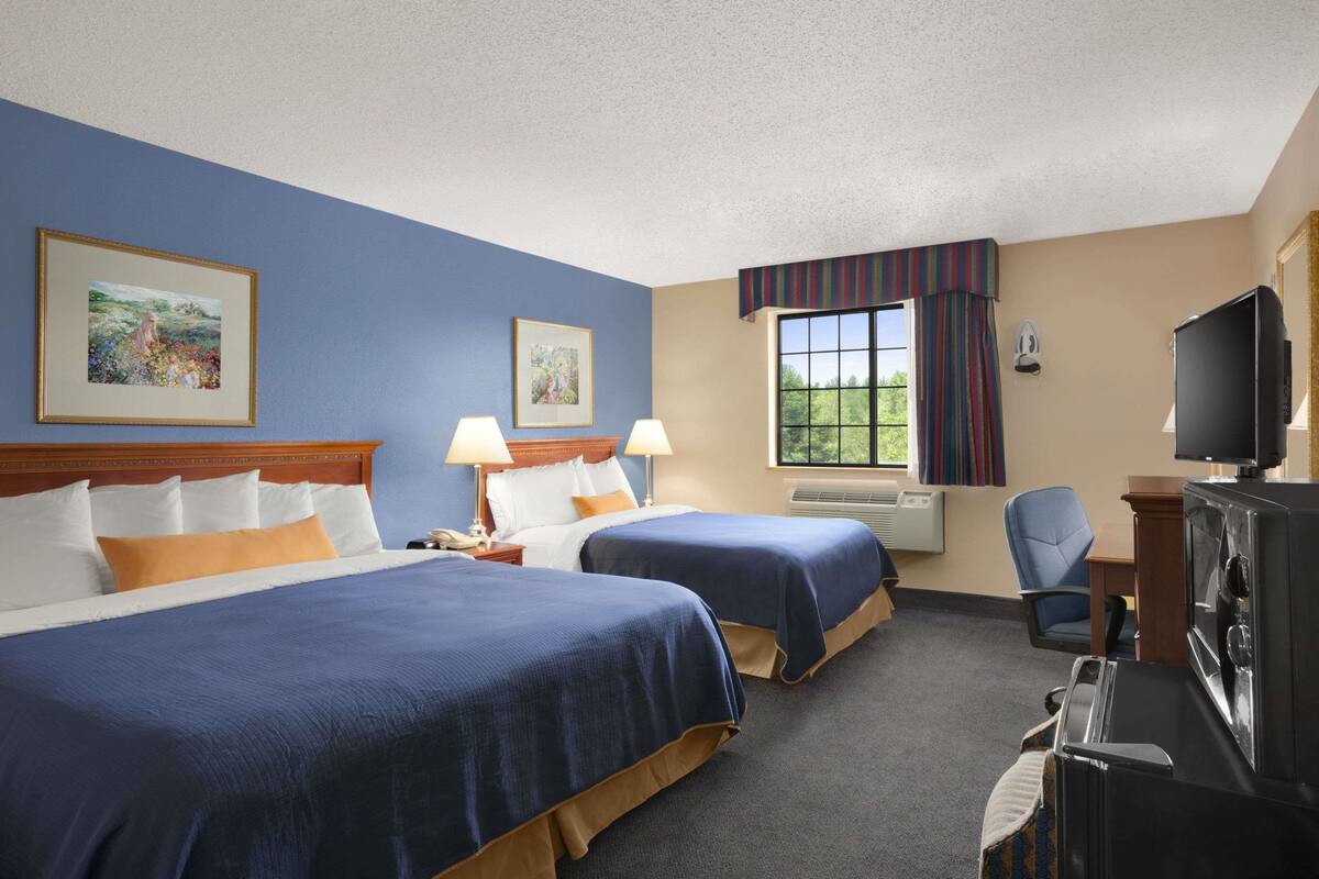 A hotel room with two beds, a television, a desk, and a window with curtains.