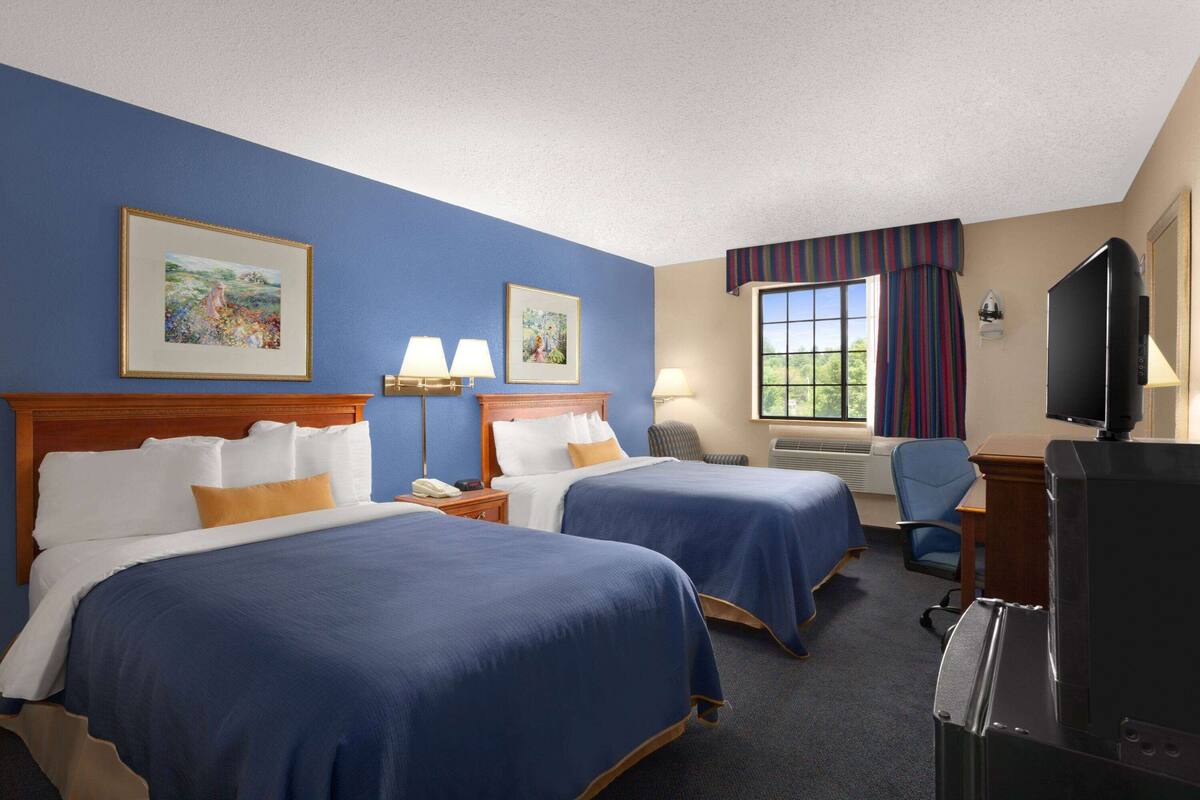 A hotel room with two beds, a TV, a desk, and a window with curtains.