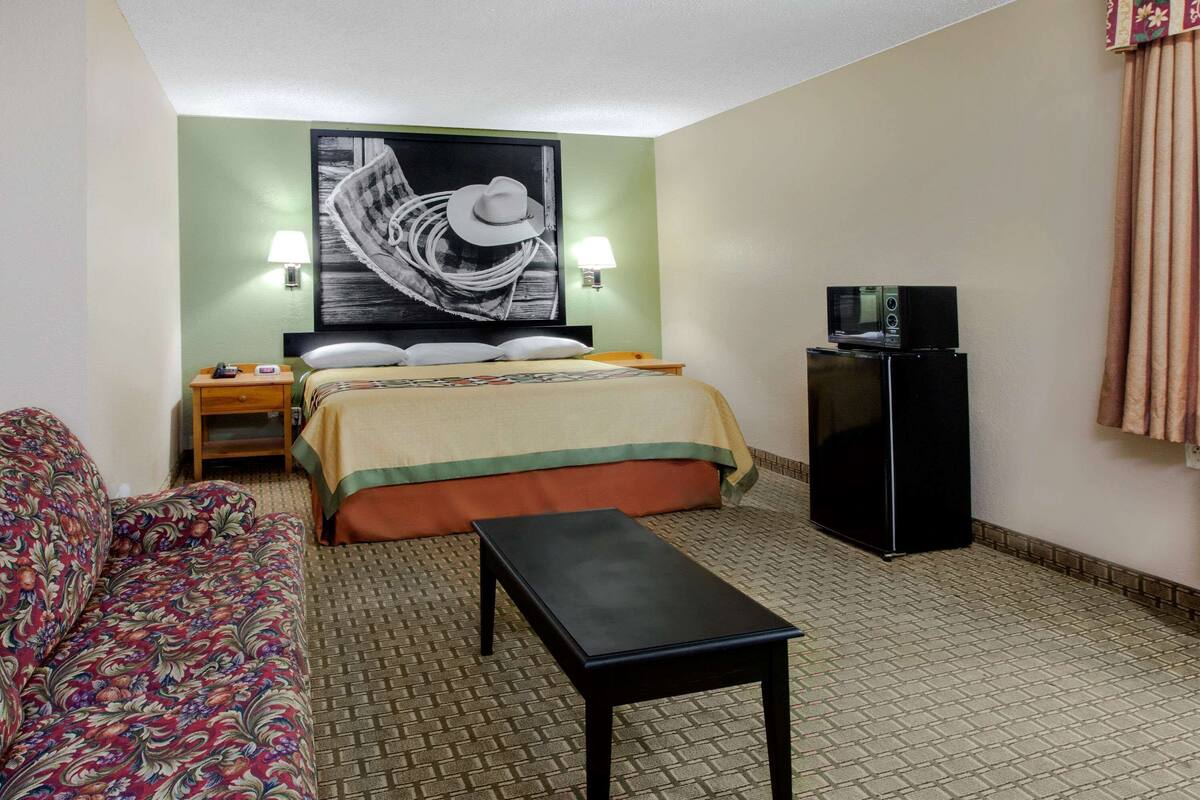Una habitación de hotel con una cama, un sofá, una mesita, un televisor en un mueble y una lámpara de pared.