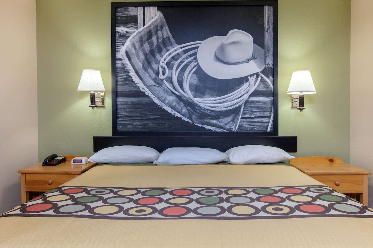 Una habitación de hotel con una cama, dos lámparas de noche, una mesita de noche con un teléfono y una obra de arte colgada en la pared.