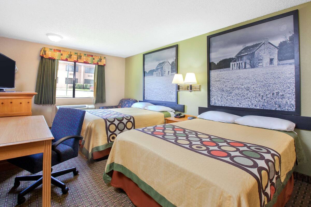 Habitación de hotel con dos camas, un escritorio, una silla, un televisor y dos lámparas fijadas a la pared.