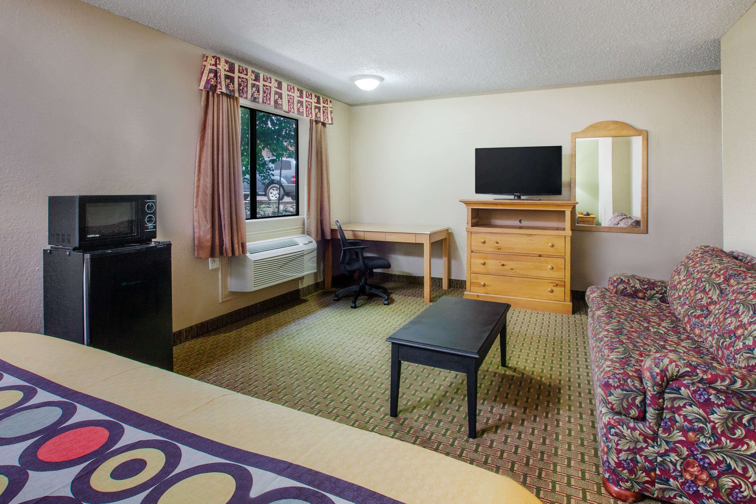 Een hotelkamer met een bed, een bureau, een stoel, een televisie, een kast en een raam met gordijnen.