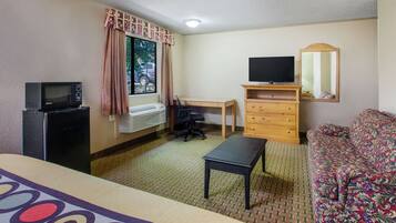 Een hotelkamer met een bed, een bureau, een stoel, een televisie, een kast en een raam met gordijnen.