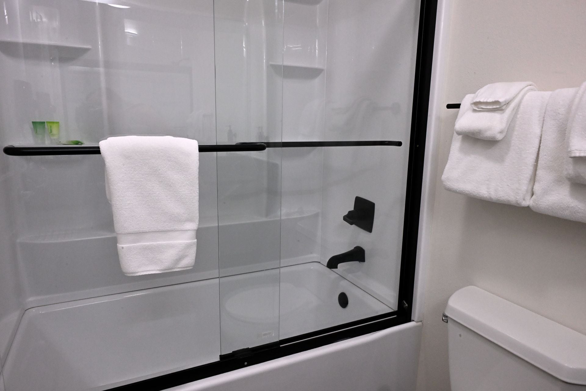 A modern bathroom with a glass-enclosed shower, a black towel rack, and a white toilet.