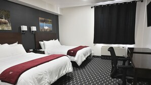 A hotel room with two beds, a desk, a chair, and a large window with a black curtain.