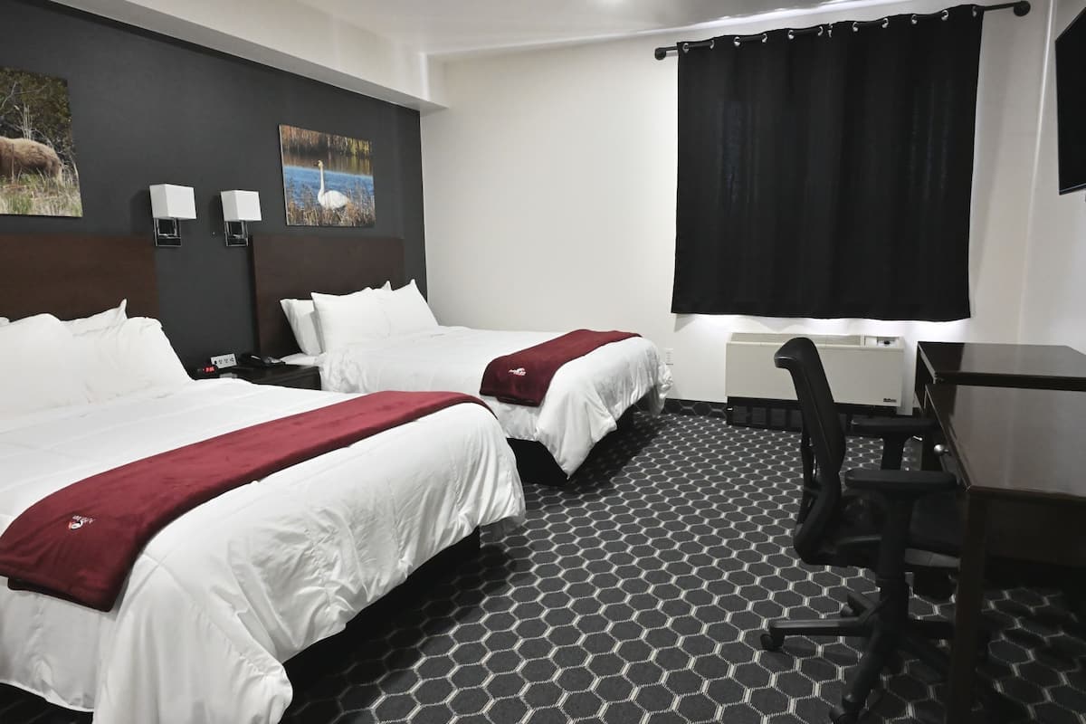 A hotel room with two beds, a desk, a chair, and a large window with a black curtain.