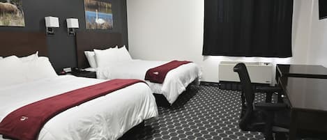 Habitación de hotel con dos camas, un escritorio, una silla y un ventanal con cortina negra.