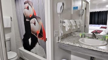 Un baño con cortina de ducha con un pingüino, un lavamanos blanco, un espejo y un perchero con varias toallas.