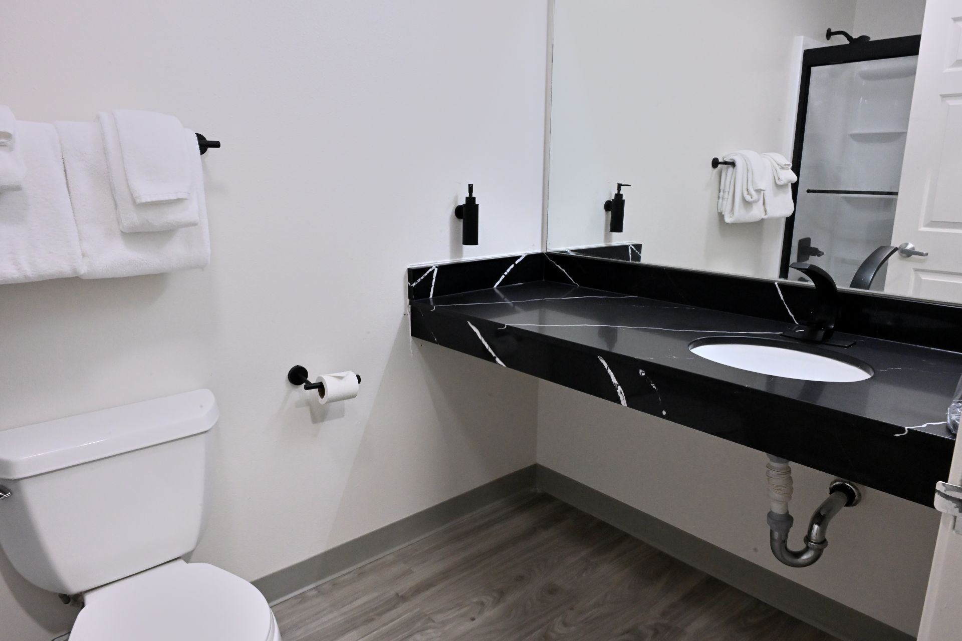 A modern bathroom with a white toilet, black marble sink, and a mirror.