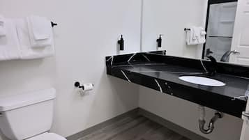 A modern bathroom with a white toilet, black marble sink, and a mirror.