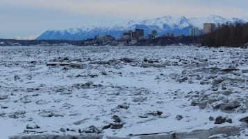 A snowy landscape with a river, ice formations, and a cityscape with mountains in the background.