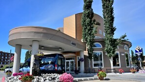 A hotel entrance with a blue van, a large column, and potted plants.