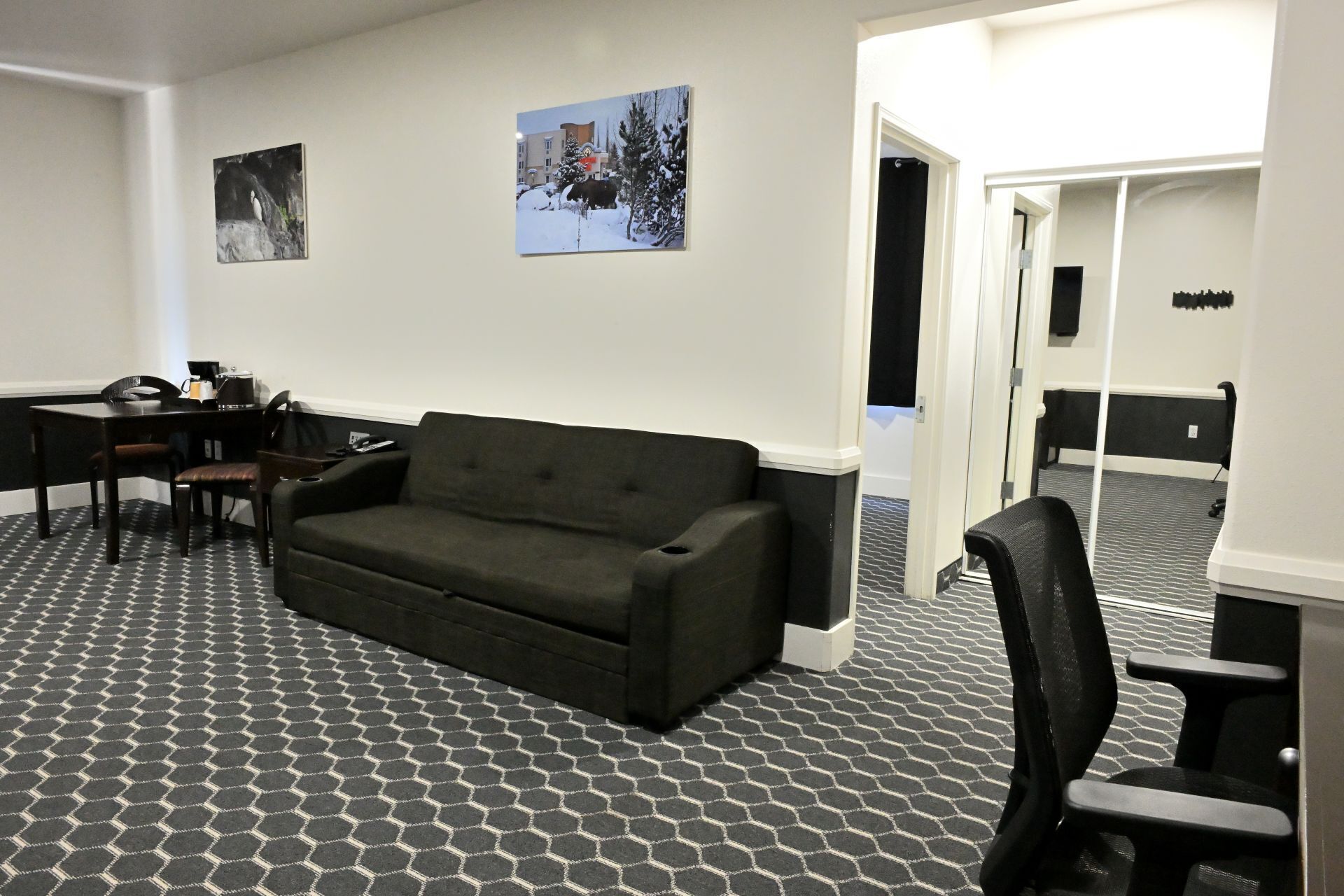 Una habitación con un sofá gris oscuro, una mesita con una silla y dos cuadros colgados en la pared.