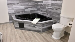 A bathroom with a black bathtub, a toilet, and grey marble tiles on the walls.