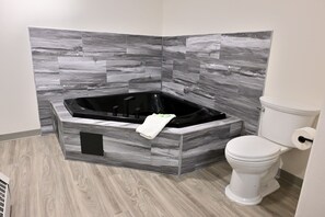 A bathroom with a black bathtub, a toilet, and grey marble tiles on the walls.