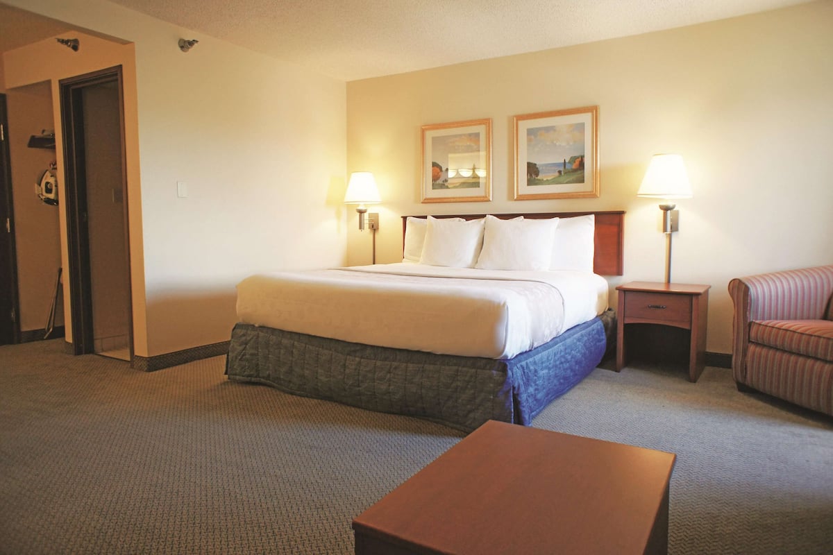A hotel room with a bed, two bedside lamps, a chair, a nightstand, and a small table.