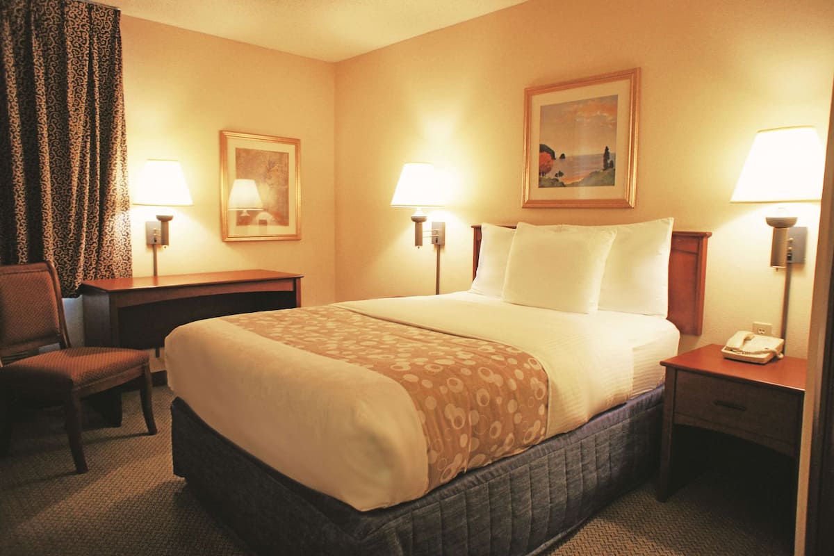 A hotel room with a bed, two bedside tables, a chair, a desk, and two lamps.