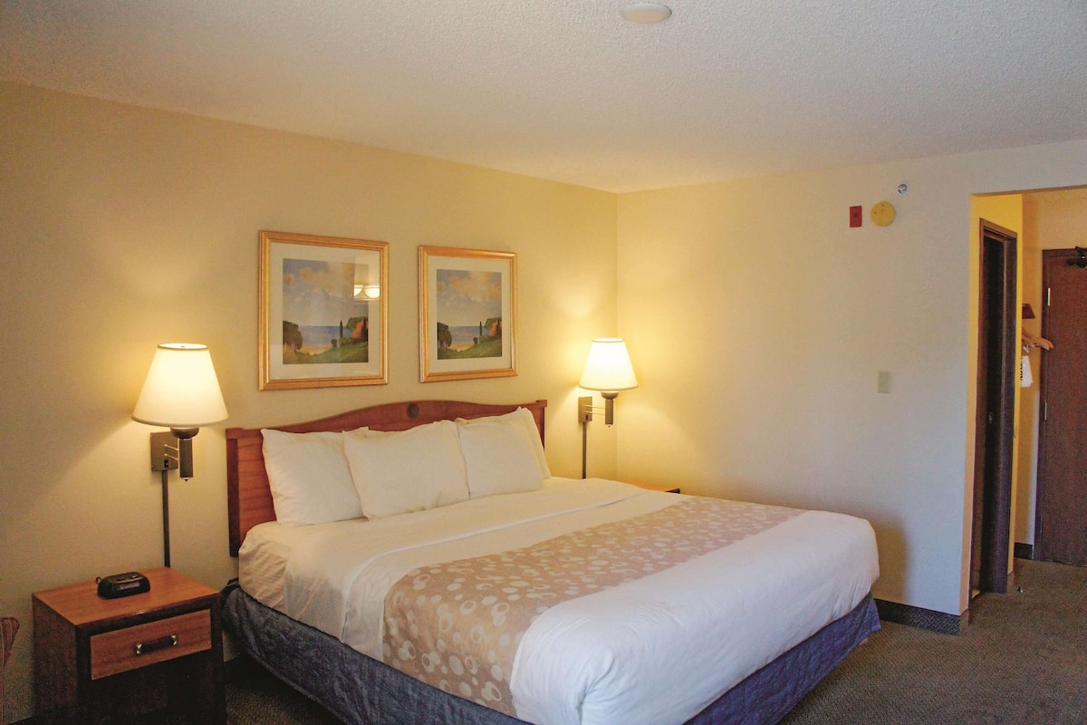 A hotel room with a large bed, two bedside lamps, a nightstand with a drawer, and two framed pictures on the wall.
