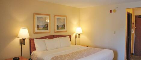A hotel room with a large bed, two bedside lamps, a nightstand with a drawer, and two framed pictures on the wall.