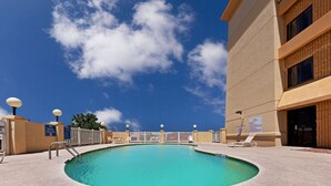 Piscina con cielo azul despejado y nubes. Hay sillas de descanso y un cartel que indica que no se permite bucear.
