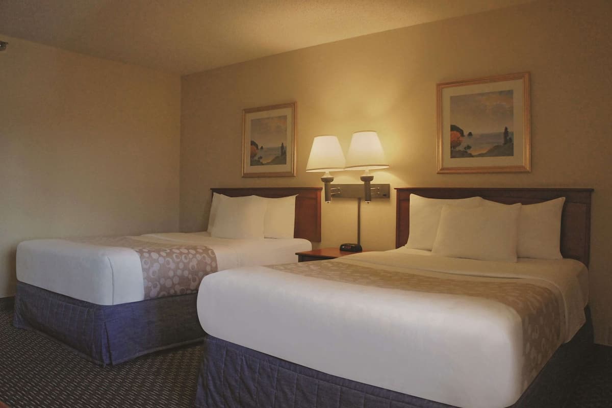 A hotel room with two beds, a nightstand, two wall-mounted lamps, and two framed pictures.