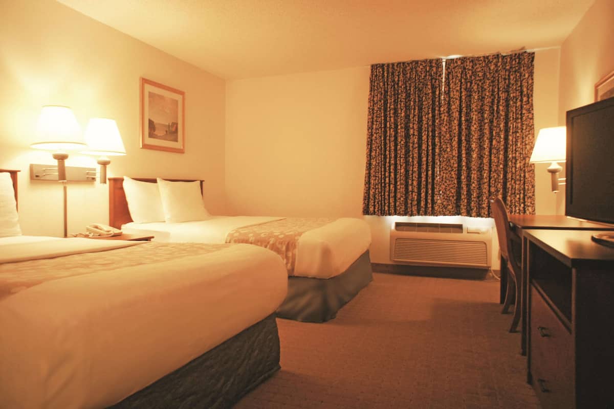 A hotel room with two beds, a desk, a television, and an air conditioning unit.