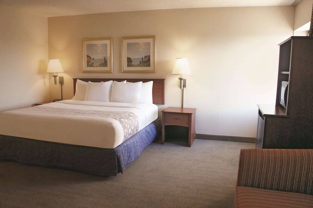 A hotel room with a large bed, two bedside lamps, a small nightstand, a chair, and two framed pictures on the wall.