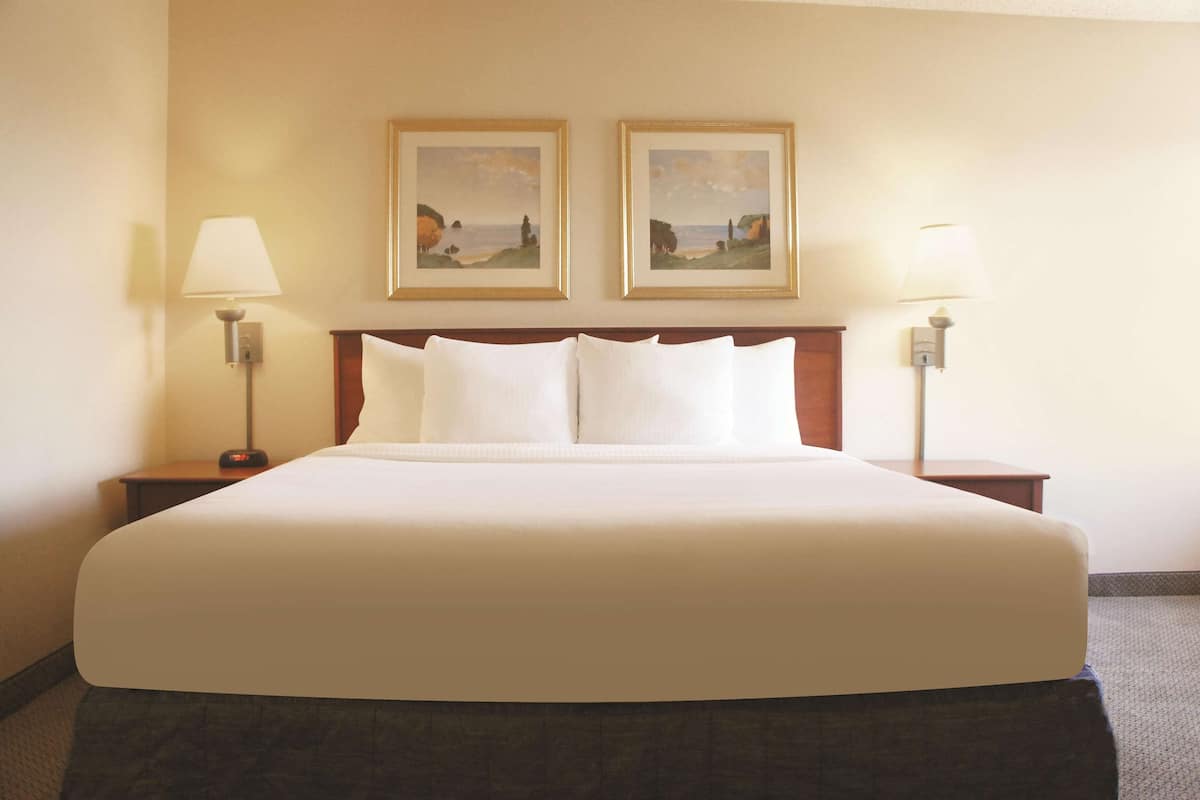 A large bed with white linens, two bedside tables with lamps, and two framed landscape paintings on the wall.