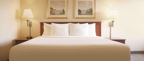 A large bed with white linens, two bedside tables with lamps, and two framed landscape paintings on the wall.