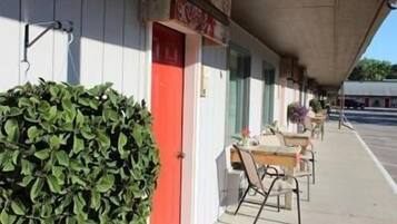 A row of tables and chairs outside a building with a red door and a green bush.