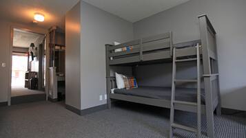 A bunk bed room with a ladder, a door leading to another room, and a carpeted floor.