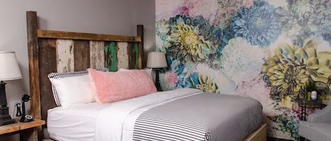 Uma cama com colcha listrada, cabeceira de madeira e um mural floral na parede.