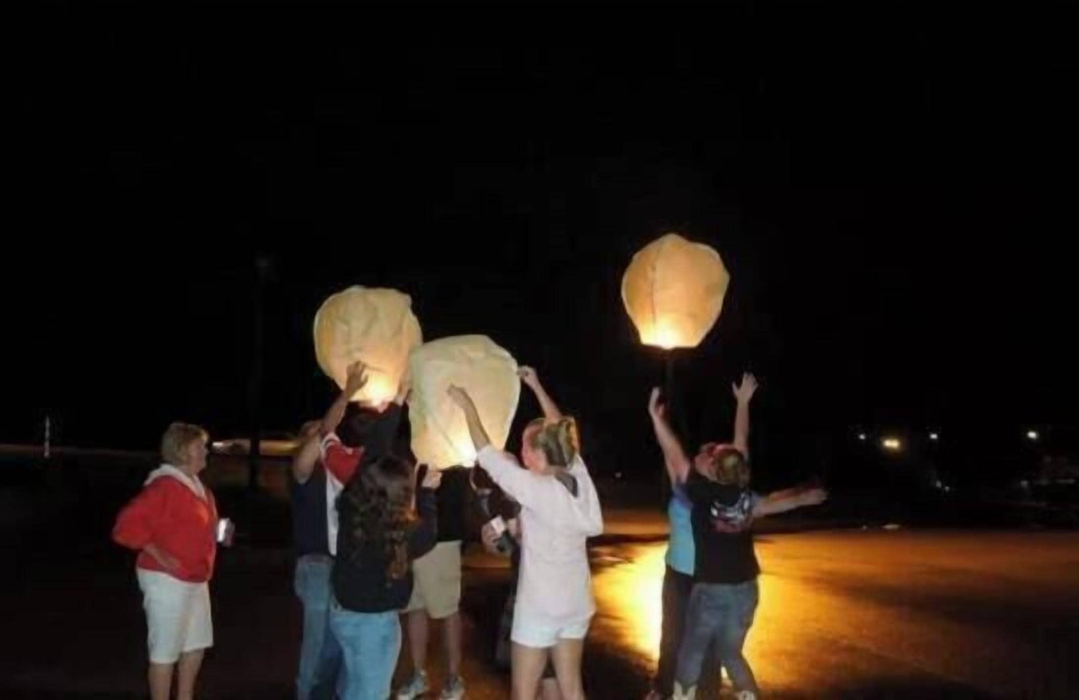 A group of people holding large paper lanterns at night.