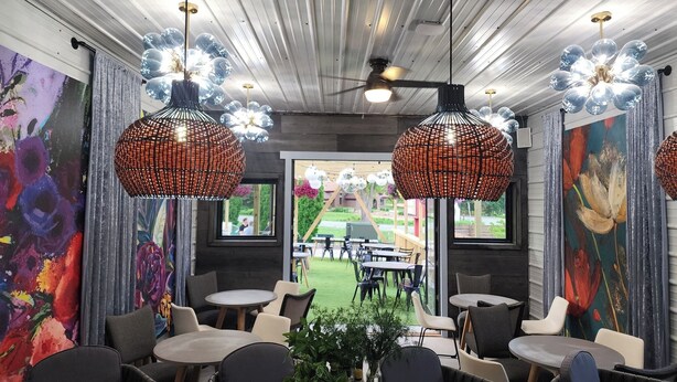 A modern dining area with round tables and chairs, decorative hanging lights, and vibrant artwork on the walls.