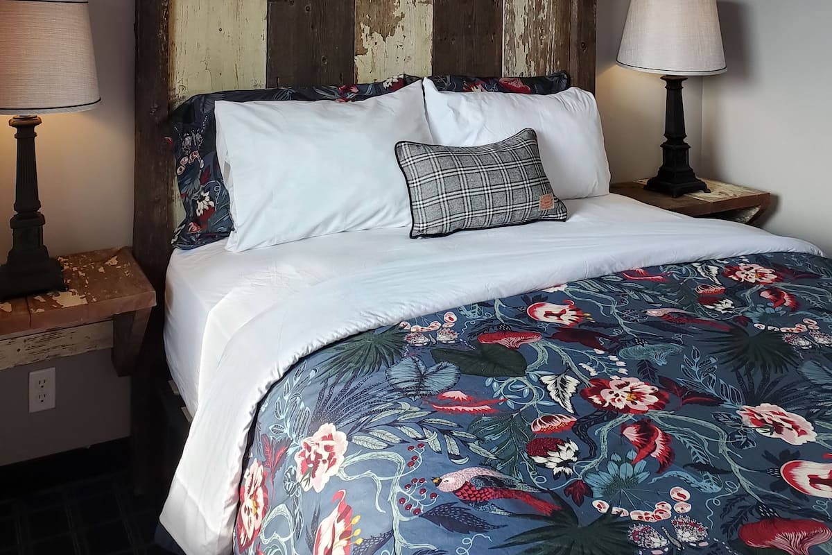 Un dormitorio con cabecera de madera, colcha estampada y dos lámparas de noche.