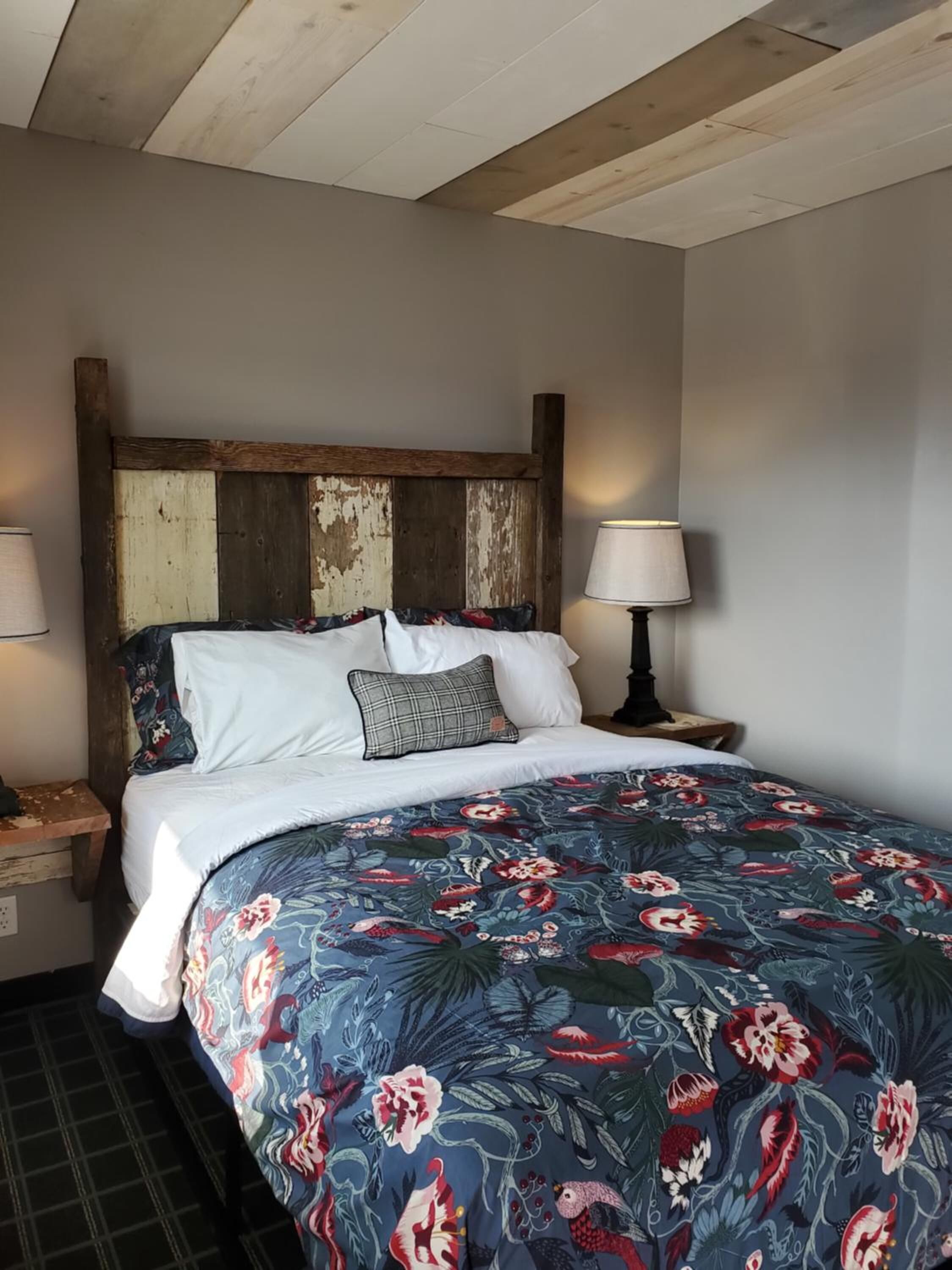 Un dormitorio con cabecera de madera, colcha estampada con motivos florales, ropa de cama blanca y dos lámparas de noche.