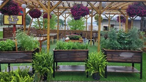 An outdoor patio area with wooden tables and benches, surrounded by planters and hanging flower baskets.