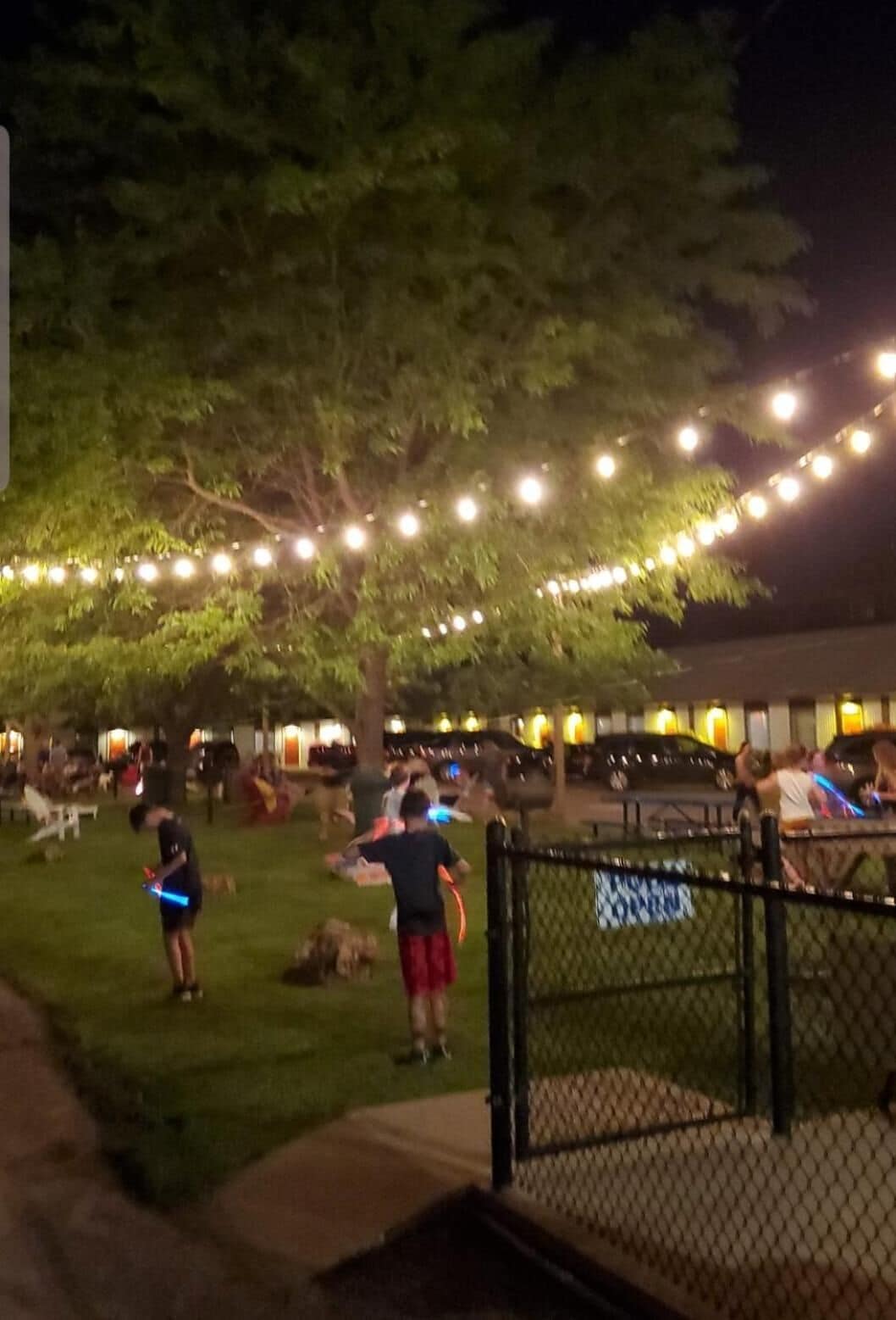 A nighttime outdoor area with string lights, a fenced area, and people.