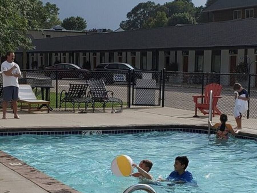 Piscina com escada de metal, espreguiçadeiras e um edifício ao fundo.