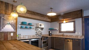 A modern kitchen with wooden beams, stainless steel appliances, and teal dishware on shelves.