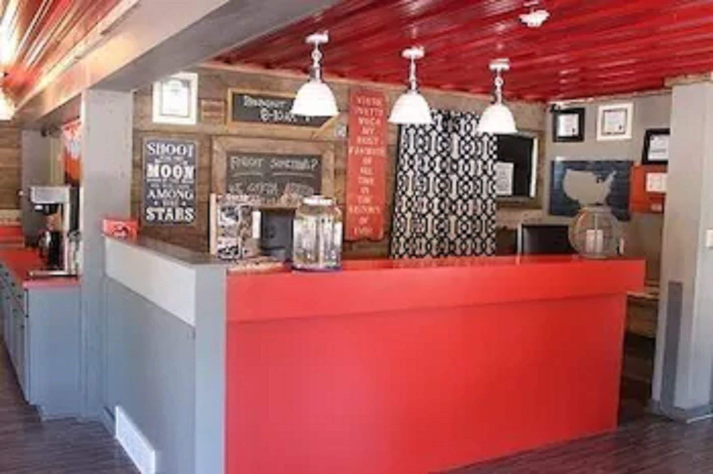A reception area with a red counter, pendant lights, and various signs including one that says "Shoot the Moon Among the Stars."